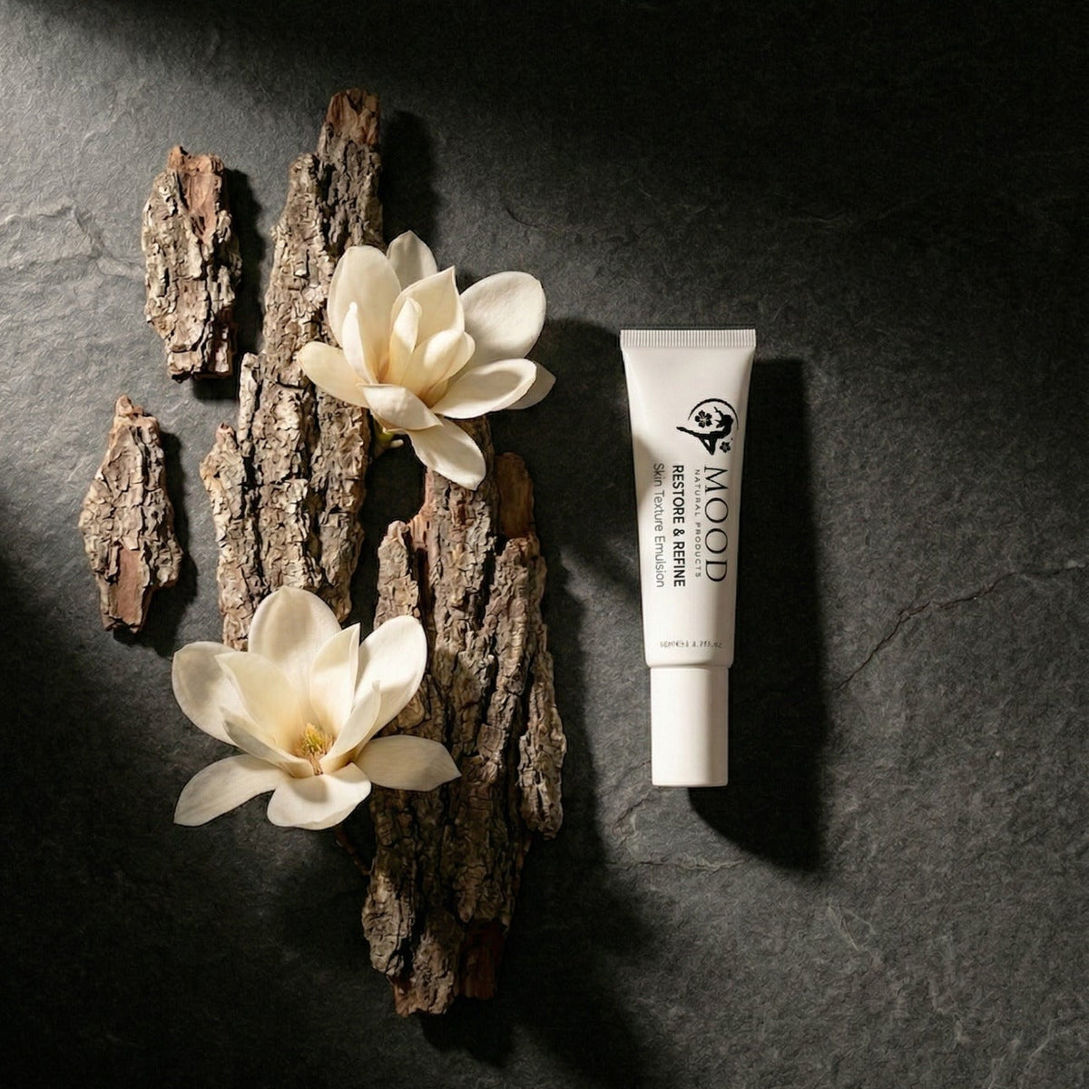 Tube auf dunklem Untergrund mit Rinde und Magnolien